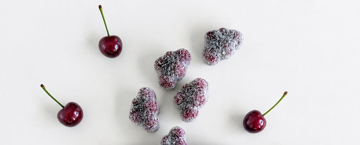 Sugared cherry gummies and fresh cherries on a white table.