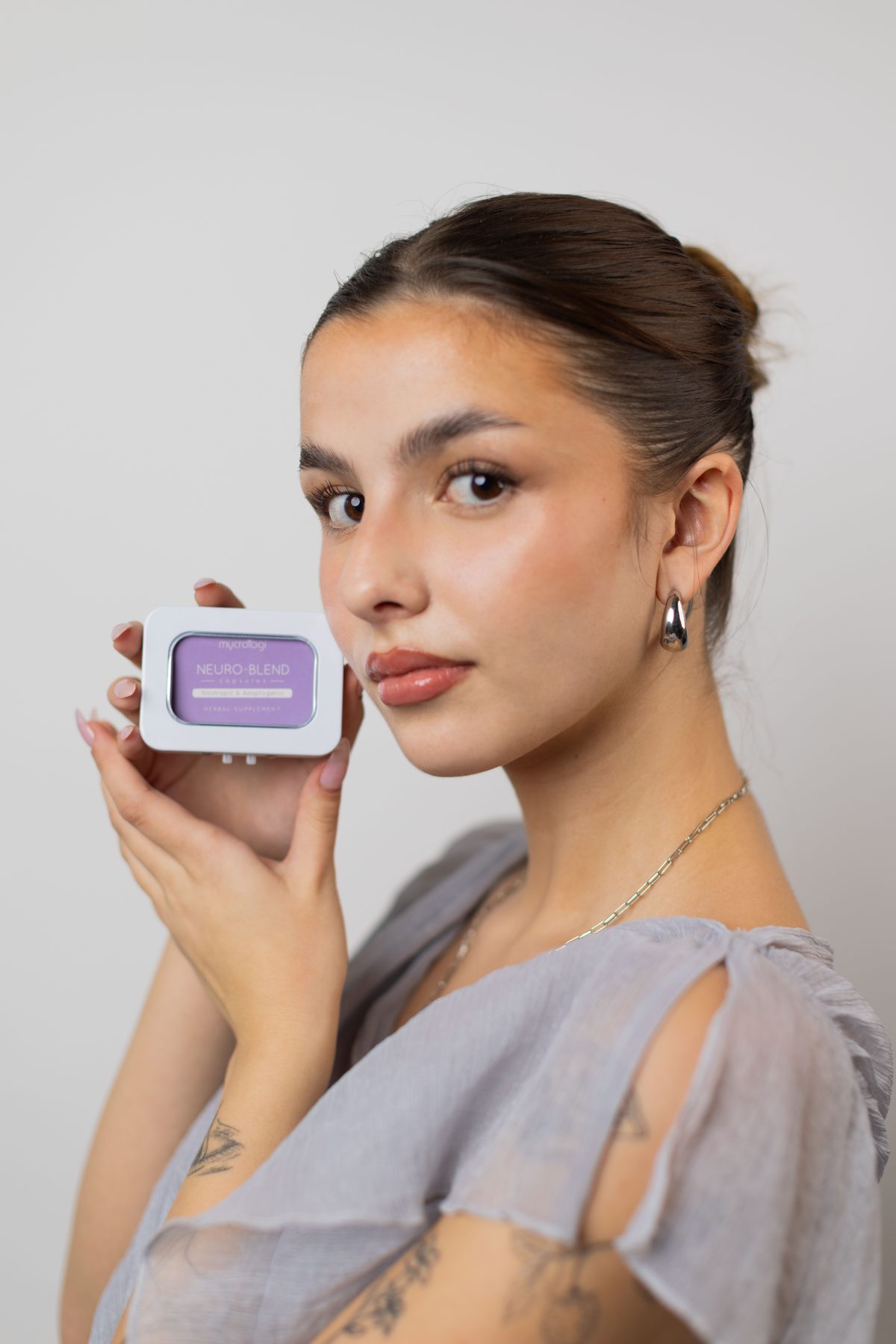 A person holding a tin of Neuro Blend against a pale studio backdrop.