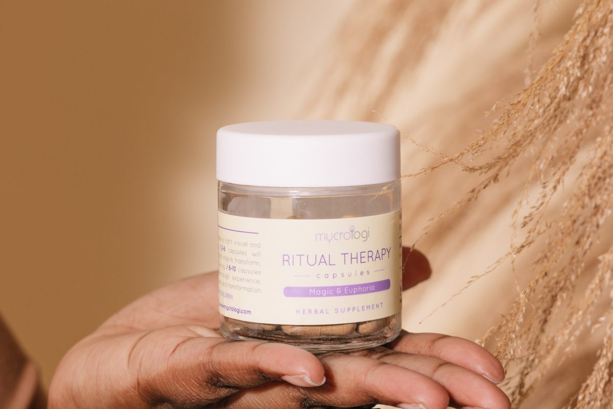 A hand holding a jar of Ritual Therapy against warm sand.