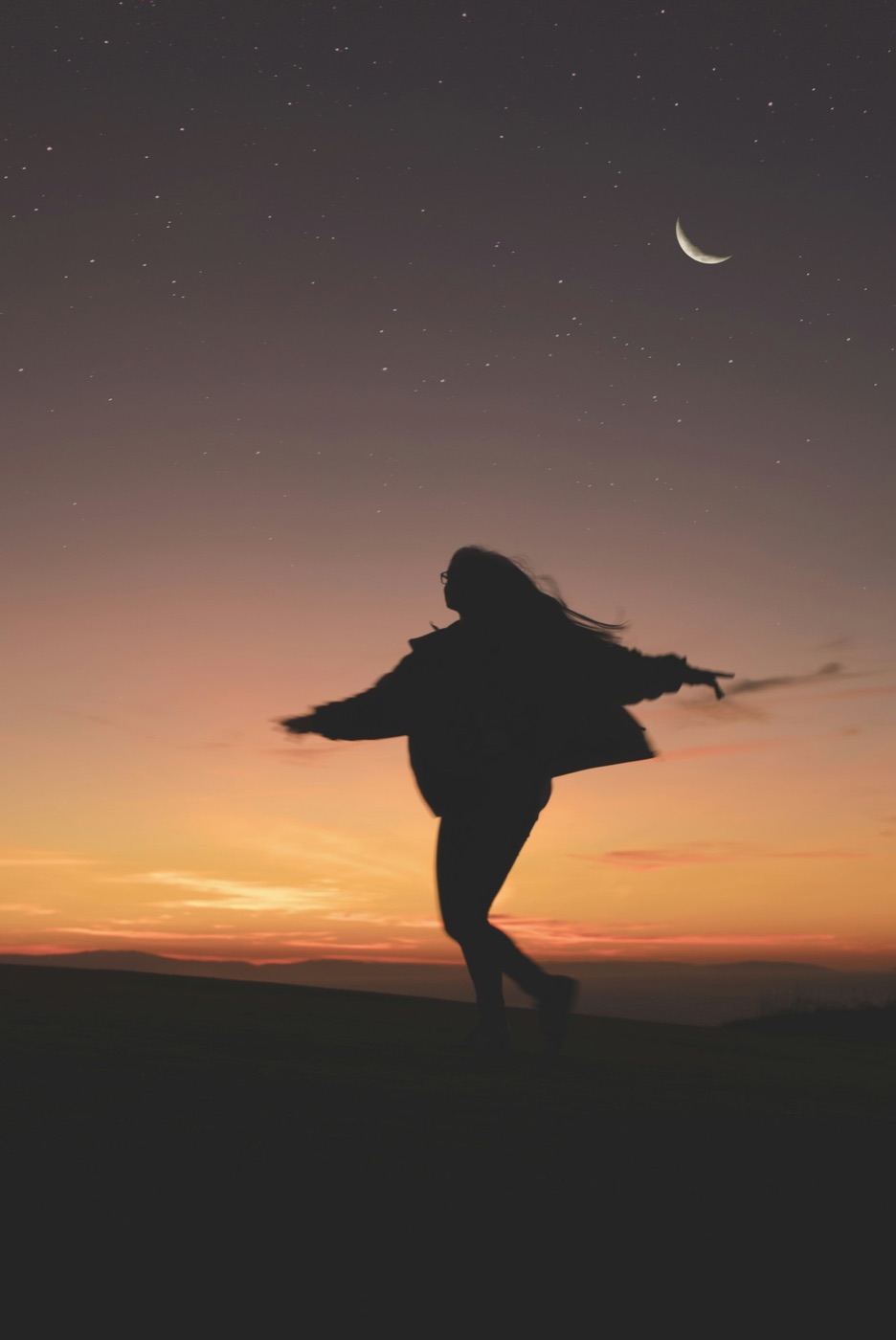 A woman dancing in silhouette at dusk beneath a crescent moon