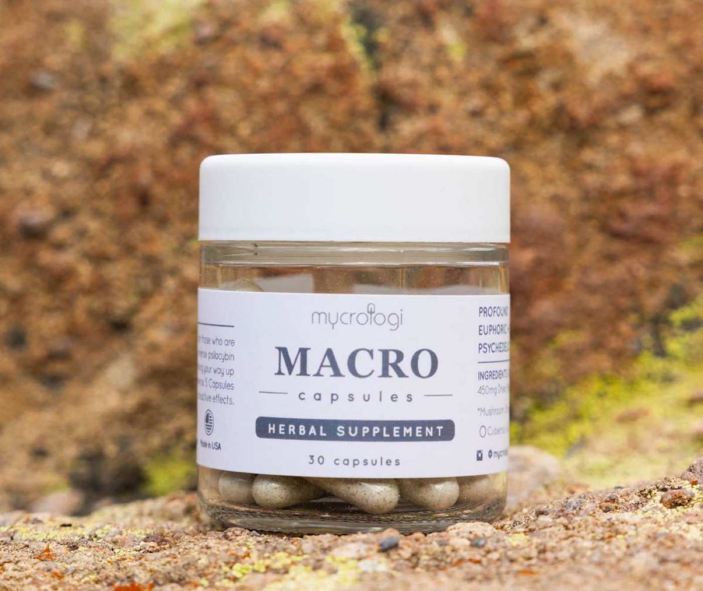A jar of Mycrologi Macro capsules resting on earth and moss