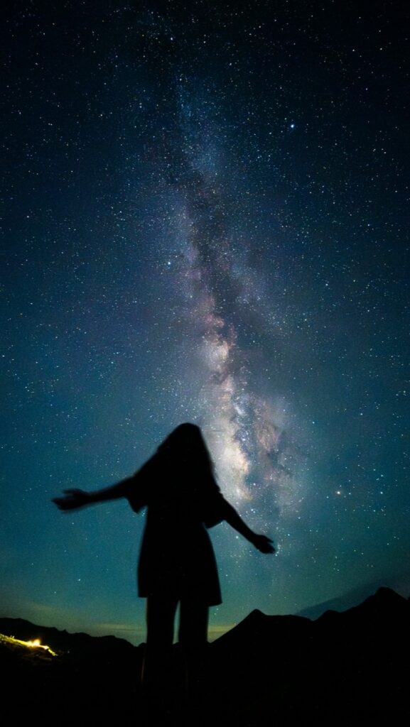 A woman in silhouette with open arms beneath the Milky Way