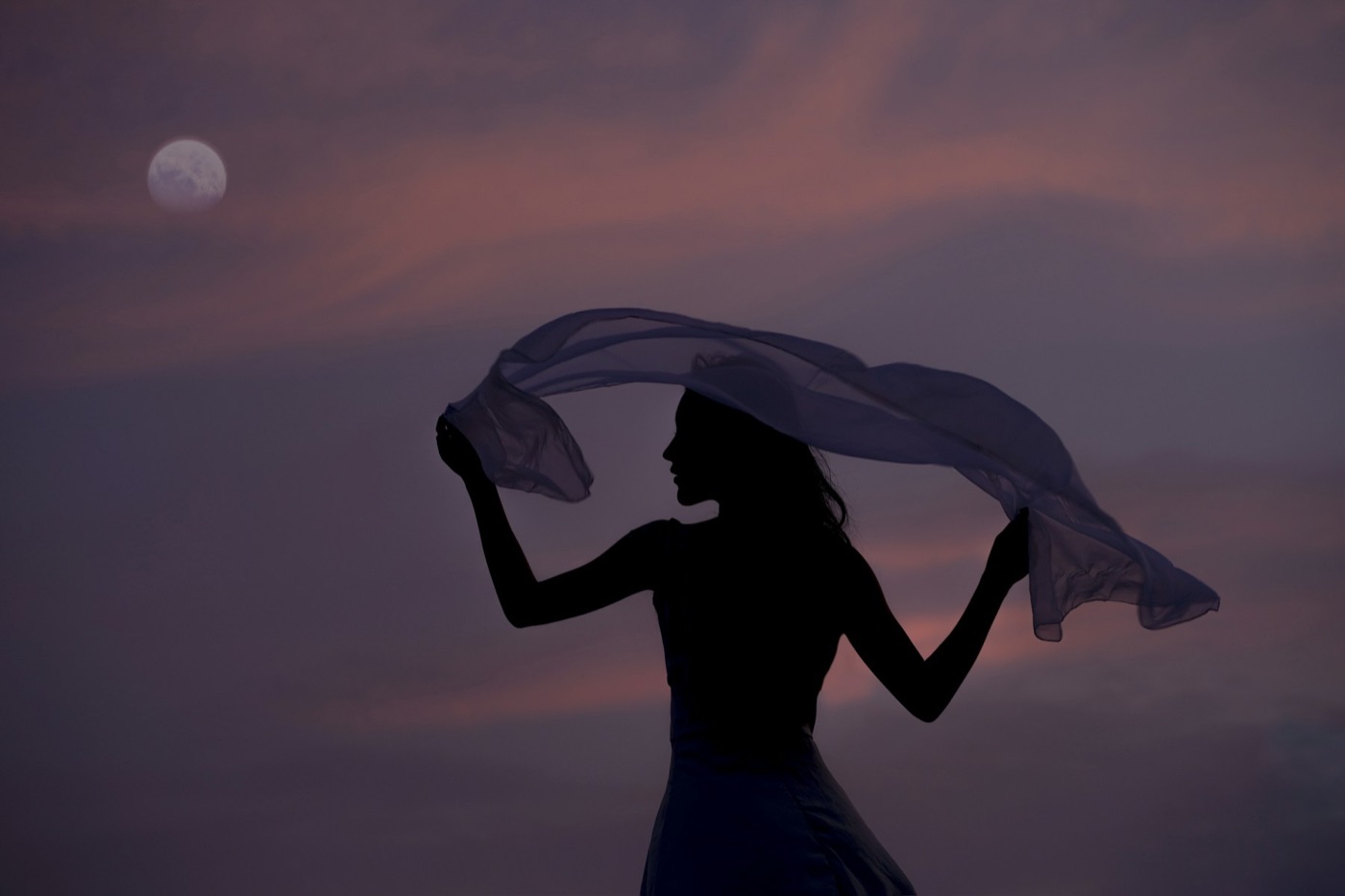 A woman in silhouette dancing with a sheer scarf beneath the moon