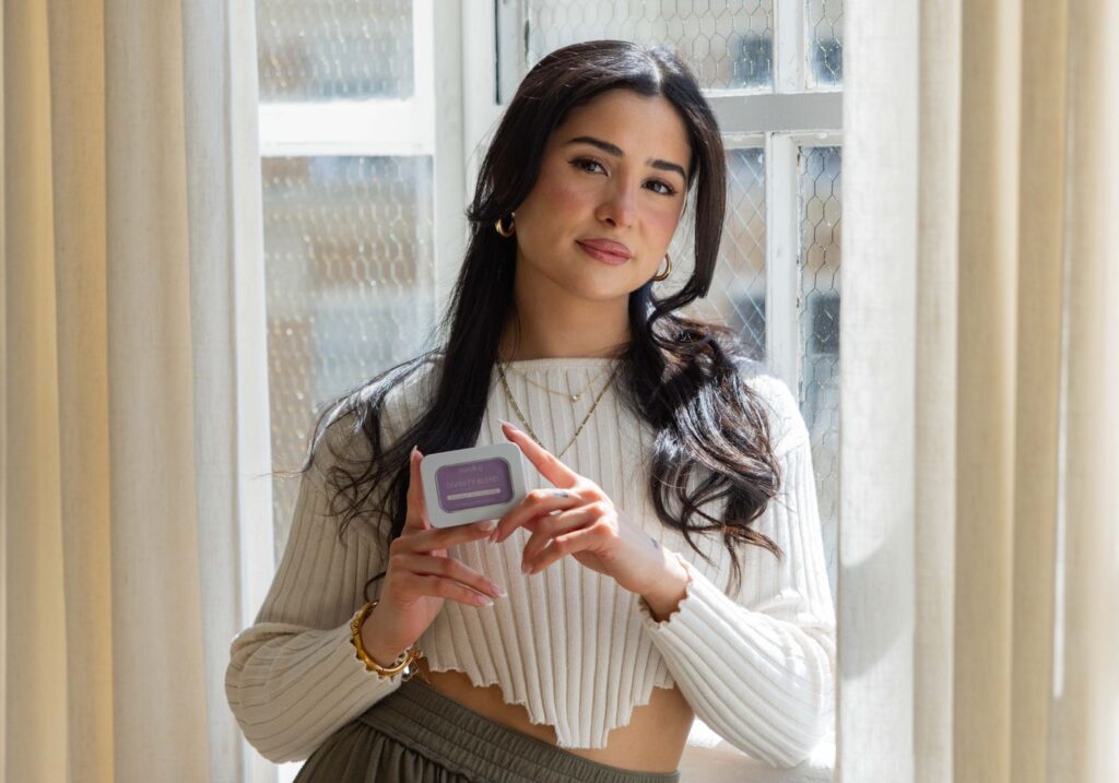 A woman in a cream knit by a sunny window holding a tin of Divinity Blend